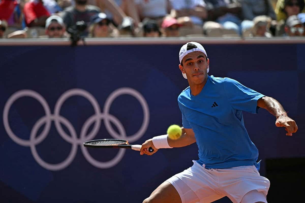 Foto de archivo: Francisco Cerúndolo, con remera celeste y gorra blanca, le pega un drive en los Juegos Olímpicos de París 2024, con los anillos olímpicos en la pared del fondo