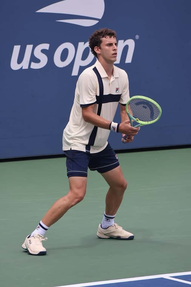 Foto de archivo: Juan Manuel Cerúndolo, con remera blanca y short azul, en posición para devolver en una cancha dura del US Open