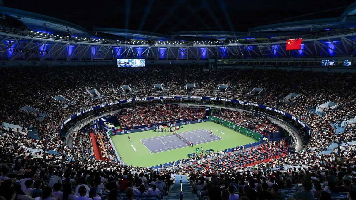 El Qi Zhong Stadium de Shanghái de noche, con las tribunas llenas, el techo iluminado en azul y un partido en juego en la cancha central