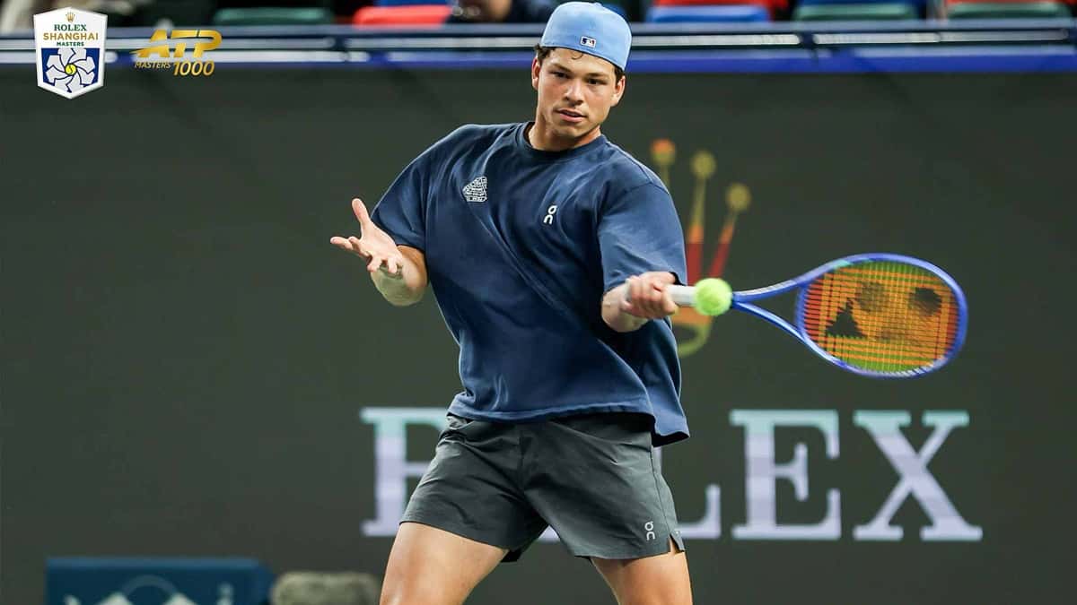 Ben Shelton, con remera azul, short gris y gorra celeste, pega un drive durante un entrenamiento en el Qi Zhong Stadium, con el logo del Rolex Shanghai Masters arriba a la izquierda