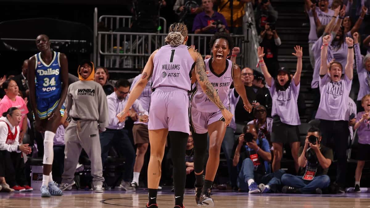 Gabby Williams, de espaldas con la camiseta 1 de Golden State Valkyries, festeja con una compañera mientras el público celebra de pie y una jugadora de Dallas Wings camina detrás