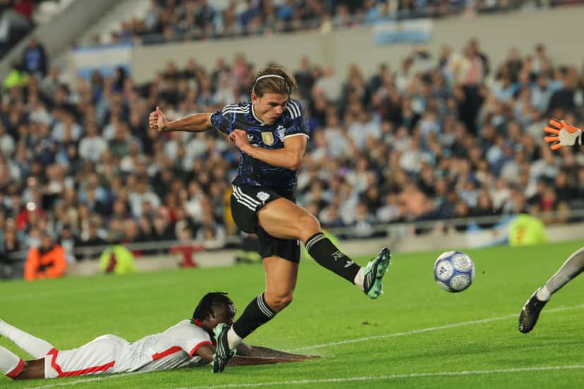 Un futbolista de la Selección Argentina remata al arco mientras un defensor de Burkina Faso queda tendido en el césped del Monumental