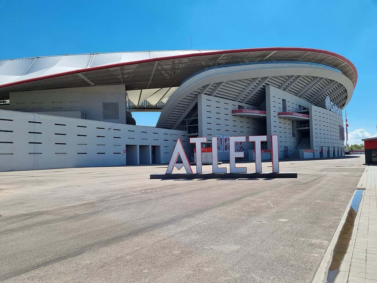 El exterior del estadio Metropolitano, del Atlético de Madrid, con el cartel gigante de letras blancas «ATLETI» delante y el cielo despejado; foto de archivo de septiembre de 2022 (foto: Cabeza2000, Wikimedia Commons, licencia CC BY-SA 4.0)