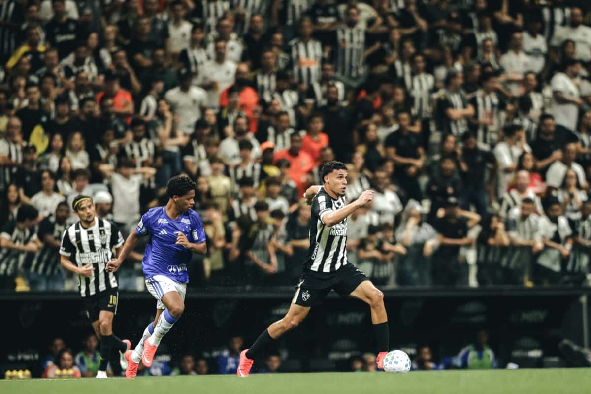 Un jugador del Atlético Mineiro, con la camiseta blanca y negra a rayas, corre con la pelota perseguido por un jugador del Cruzeiro, de camiseta violeta, con la tribuna llena del Arena MRV detrás, en el clásico del jueves 29 de octubre de 2026 (foto: Pedro Souza, prensa Clube Atlético Mineiro)