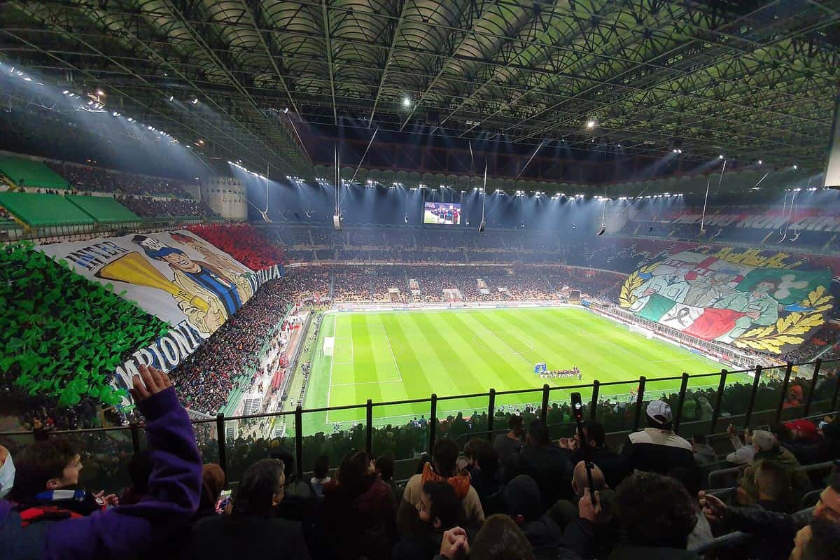 Las tribunas del estadio San Siro, en Milán, llenas de hinchas con banderas y un mosaico en la previa de un derbi entre Milan e Inter; foto de archivo de noviembre de 2021 (foto: Milanellopv, Wikimedia Commons, licencia CC BY-SA 4.0)