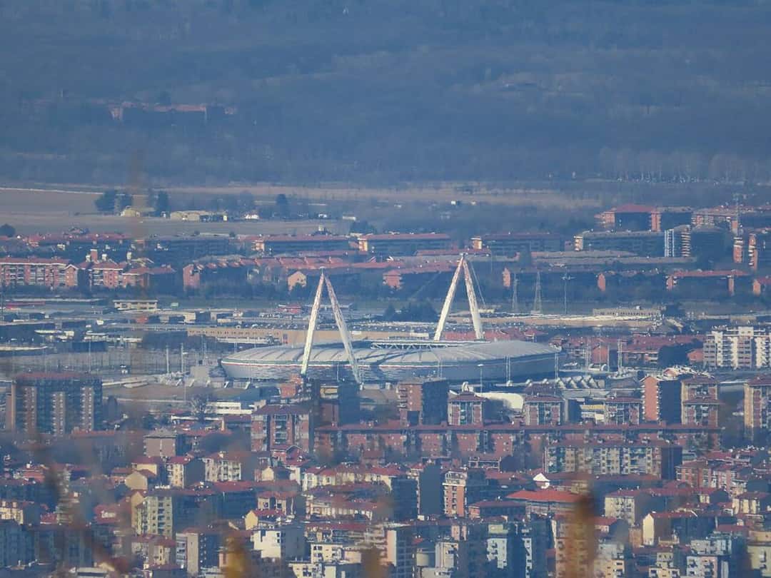 El estadio de Juventus visto desde la colina de la Maddalena, en Turín, con sus mástiles blancos sobre el barrio; foto de archivo de 2020 (foto: Matteo Aresca 05, Wikimedia Commons, licencia CC BY-SA 4.0)