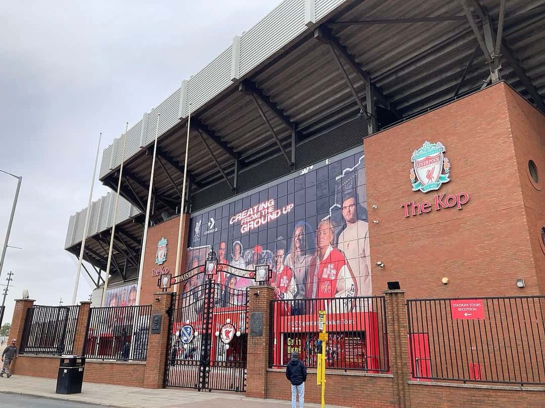 El frente de la tribuna del Kop sobre Walton Breck Road, con el escudo del Liverpool y los portones Paisley Gateway; foto de archivo de abril de 2023 (foto: Vojta.zurek, Wikimedia Commons, licencia CC BY-SA 4.0)