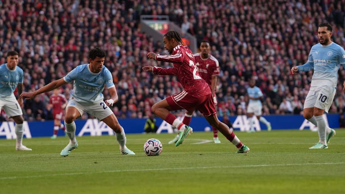 Bradley Barcola, con la camiseta roja del Liverpool, encara con la pelota a Matheus Nunes, de celeste, mientras Rayan Cherki sigue la jugada en Anfield (foto: Liverpool FC)
