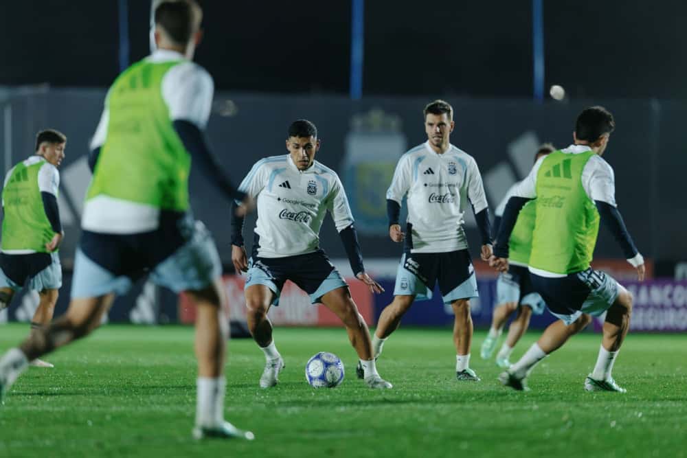 Jugadores de la Selección Argentina con ropa de entrenamiento y pecheras verdes disputan una pelota en una práctica nocturna en el predio de Ezeiza (foto oficial de la AFA)