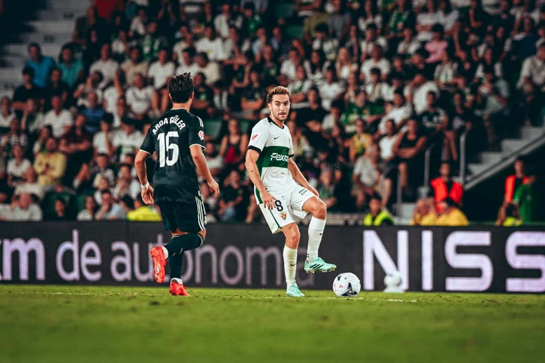 Un jugador del Elche, con la camiseta blanca y verde número 8, maneja la pelota ante un rival de camiseta negra; foto de archivo (foto: Elche CF)