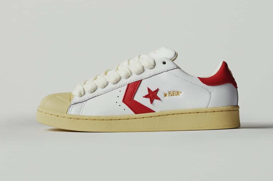 Converse Pro Leather blanca de GOLF le FLEUR* de perfil sobre fondo gris claro, con cuero blanco, la estrella y el chevron rojos, talón rojo, cordones gruesos color crudo y puntera de goma