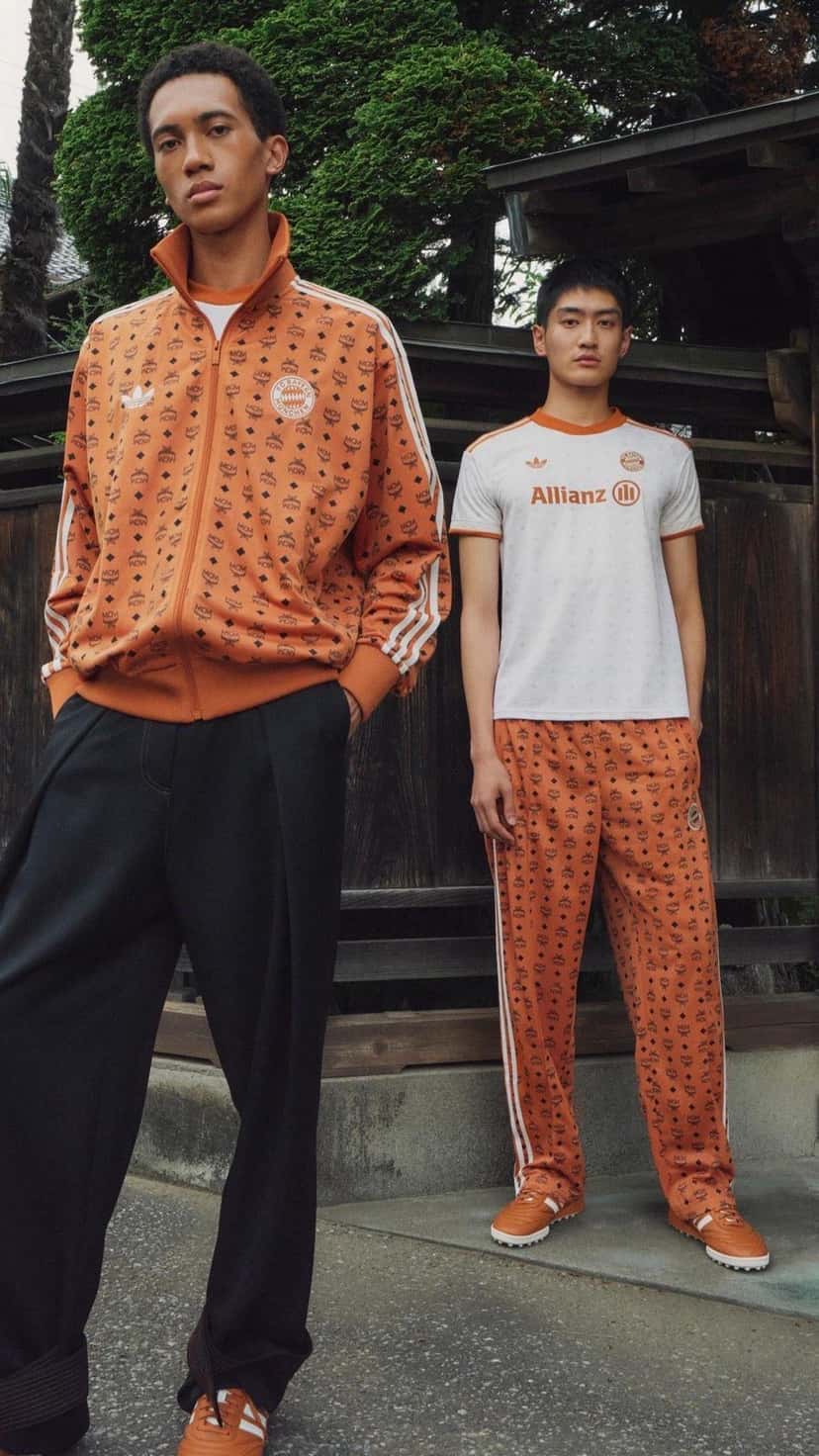 Dos hombres con prendas de la colección MCM x FC Bayern x adidas: campera deportiva coñac con el monograma de MCM y camiseta blanca, con zapatillas coñac