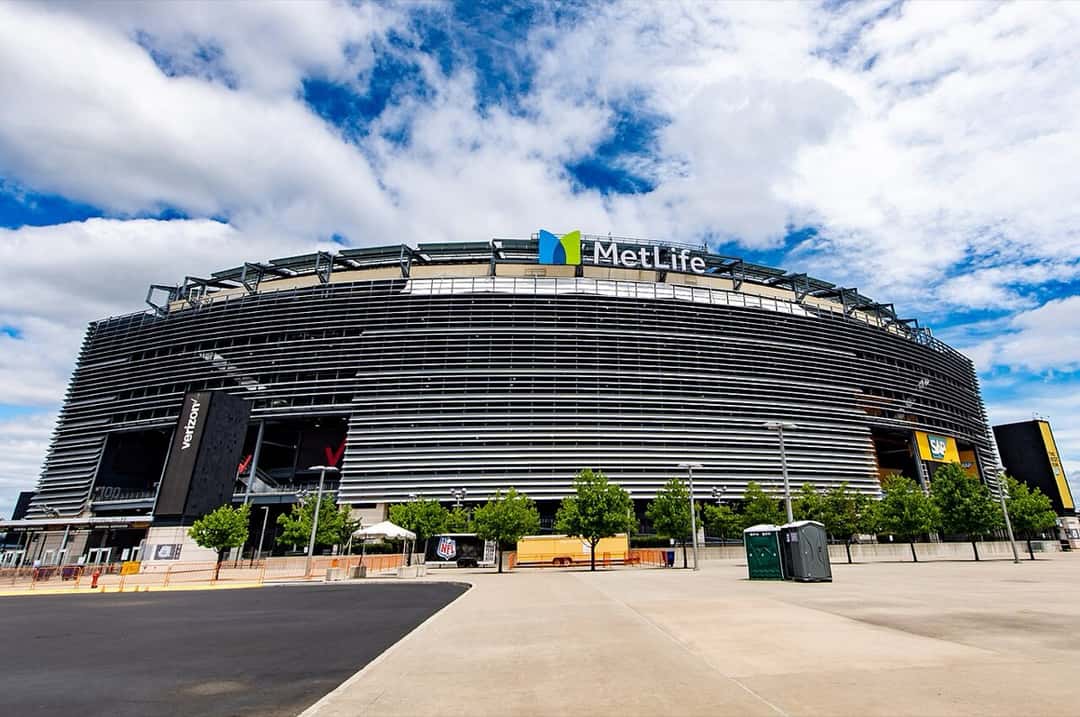 Fachada del MetLife Stadium de East Rutherford, Nueva Jersey, con su revestimiento de láminas metálicas y el cartel de MetLife arriba, en un día de cielo con nubes. Foto: Thecoolone1223, Wikimedia Commons, CC BY 4.0