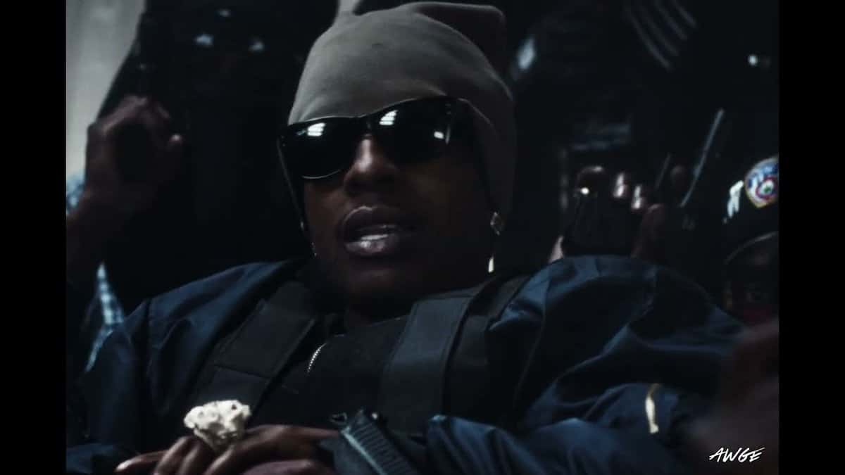 Fotograma del video oficial de «SWAT TEAM»: A$AP Rocky, con gorro gris, anteojos negros y chaleco táctico oscuro, rodeado de gente en una escena de poca luz