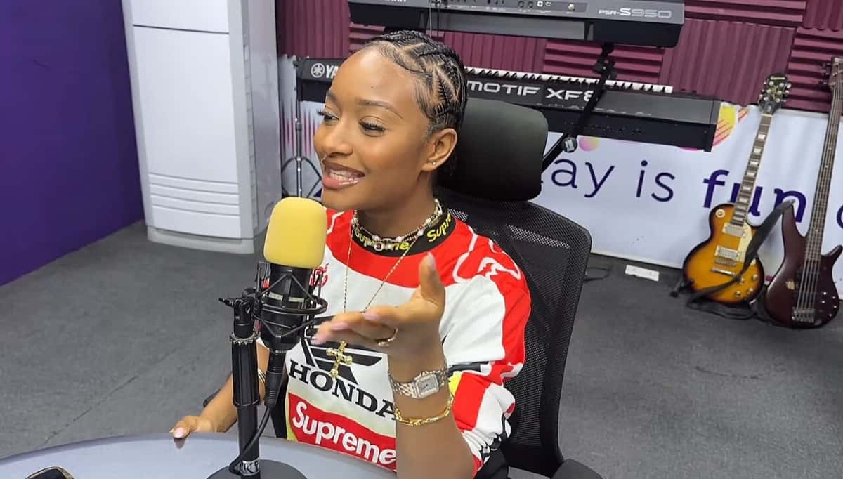 Ayra Starr sonríe frente a un micrófono en un estudio de radio de Lagos, con trenzas recogidas, collares y una remera roja y blanca, con teclados y guitarras de fondo (foto de archivo)