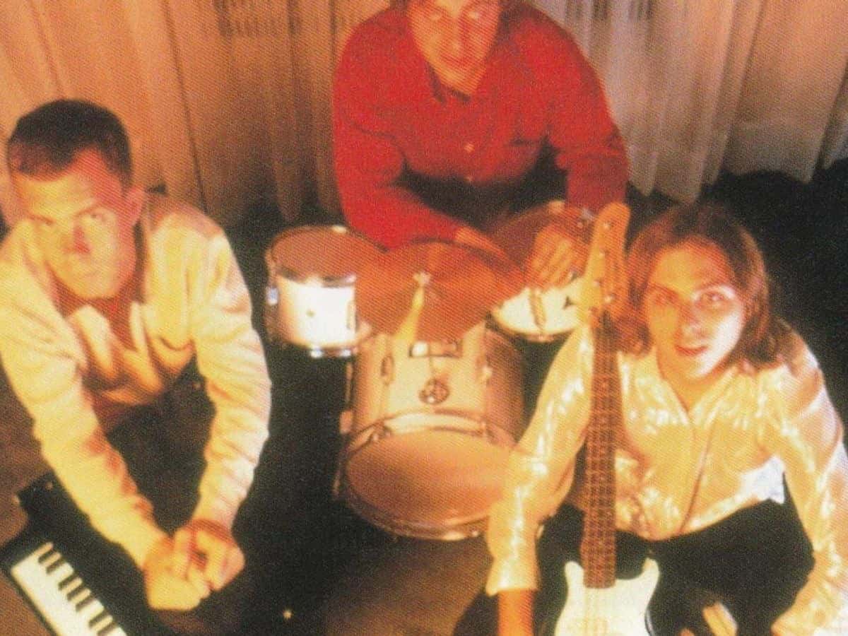 Foto de prensa de archivo de Ben Folds Five en los noventa: los tres integrantes alrededor de una batería, con un bajo y un teclado, en una habitación con cortinas