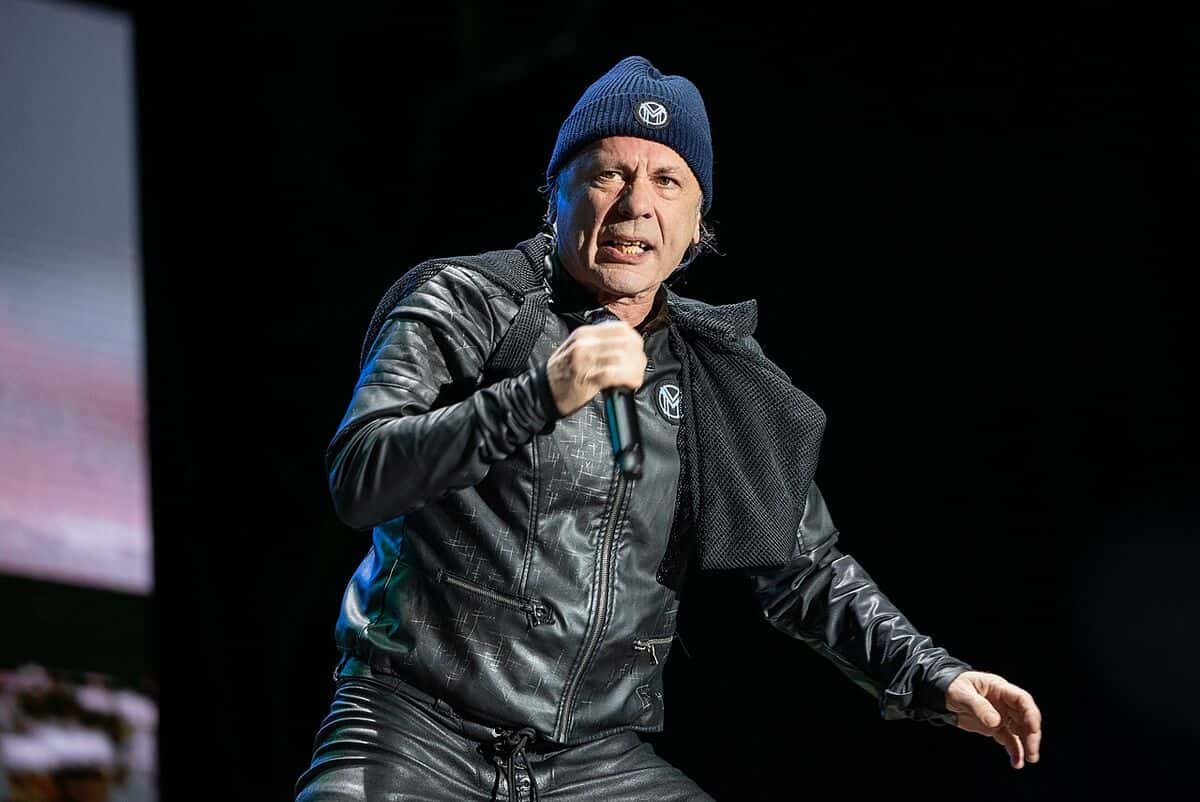 Bruce Dickinson, con gorro azul y campera de cuero negra, canta con el micrófono en la mano en un show de «The Mandrake Project» en 2024 (foto de archivo)