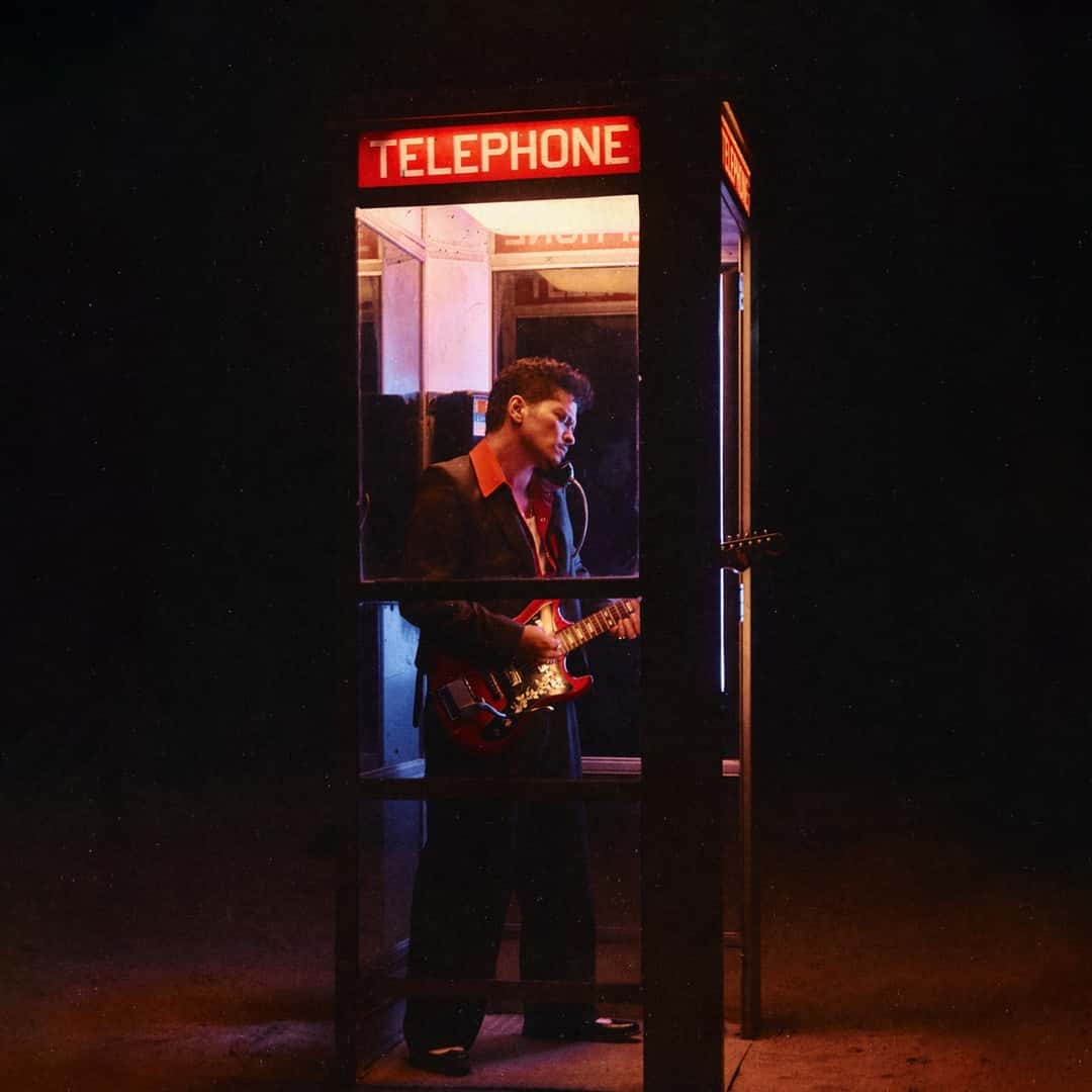 Portada del single Dance With Me de Bruno Mars: el cantante toca una guitarra eléctrica roja dentro de una cabina telefónica iluminada de noche