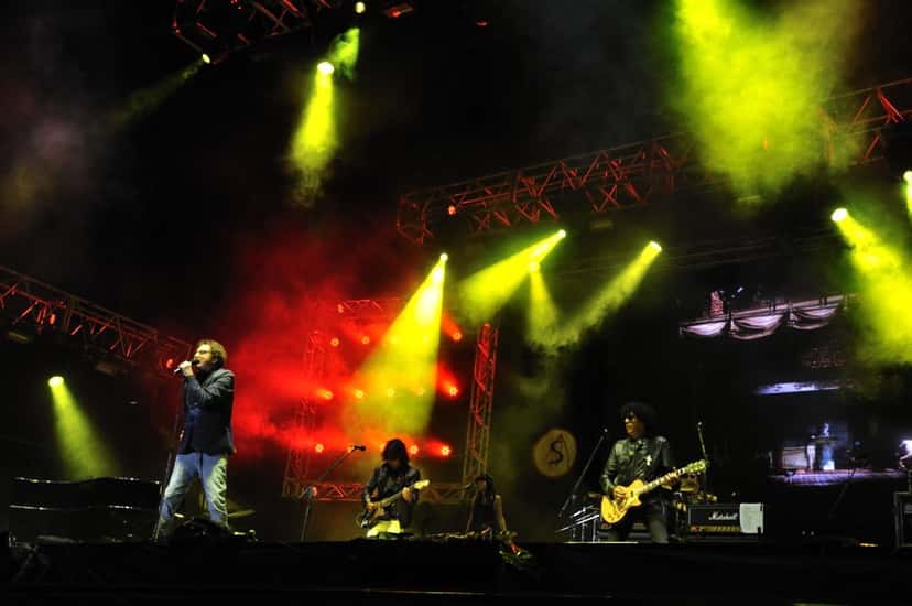 Charly García canta en el escenario de Cosquín Rock 2011, con luces verdes, amarillas y rojas y su banda detrás (foto de archivo). Foto: dandrez, CC BY-SA 2.0, vía Wikimedia Commons