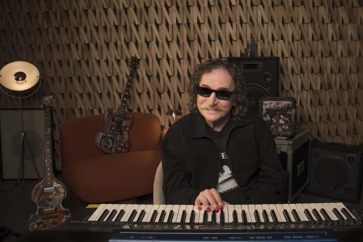 Charly García con anteojos negros toca un teclado en un estudio con guitarras y un bajo colgados detrás, en una imagen del anuncio oficial de Netflix