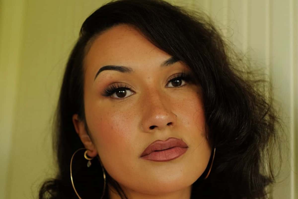 Foto de prensa de Cleo Sol: primer plano de la cantante con pelo oscuro por los hombros y aros grandes, frente a una pared verde clara