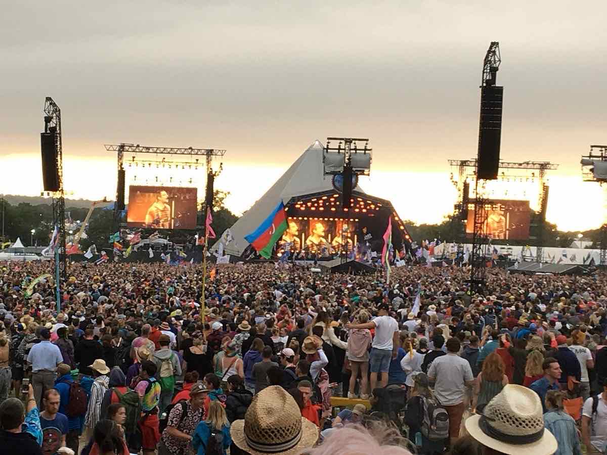 Foto de archivo de Glastonbury 2019: una multitud con sombreros y banderas frente al Pyramid Stage, el escenario principal con forma de pirámide, al atardecer y con pantallas gigantes a los costados