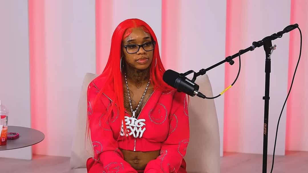 Sexyy Red, con pelo rojo largo, anteojos y conjunto rojo, sentada frente a un micrófono durante una entrevista en diciembre de 2023 (foto de archivo). Foto: Million Dollaz Worth of Game, CC BY 3.0, vía Wikimedia Commons
