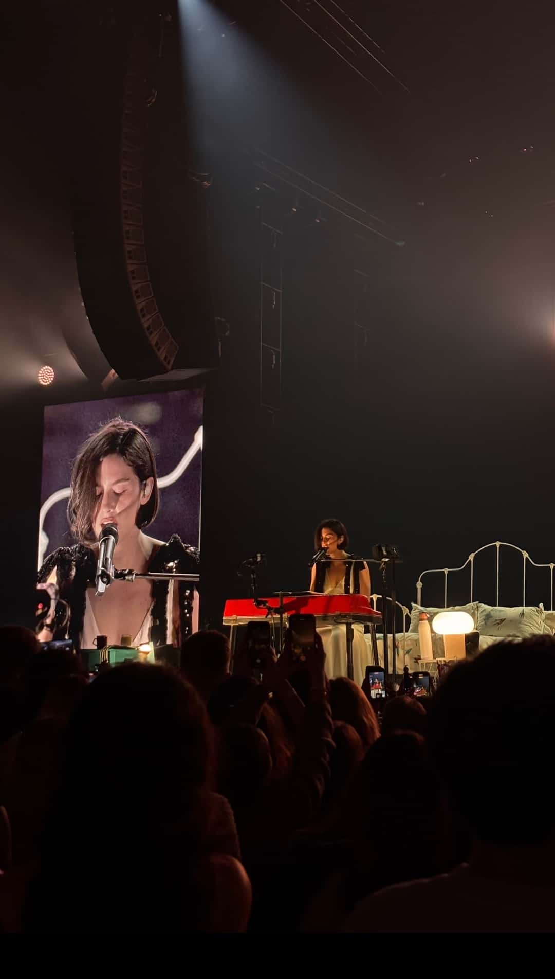 Gracie Abrams en vivo en Madrid en febrero de 2025, durante «The Secret of Us Tour»: la cantante toca un teclado rojo en el escenario, con su imagen en una pantalla gigante a la izquierda y el público en primer plano (foto de archivo). Foto: Nataliaagalvez, CC BY 4.0, vía Wikimedia Commons