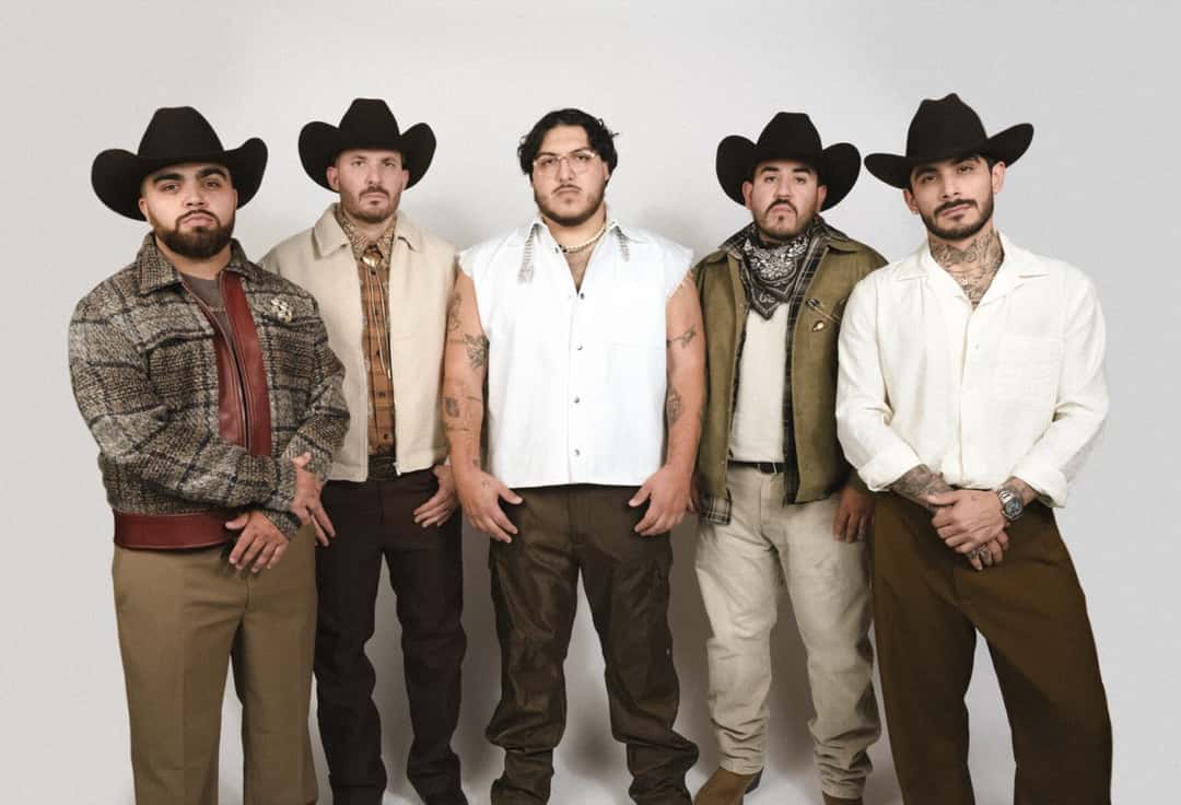 Foto de prensa de Grupo Frontera: los cinco integrantes de pie frente a un fondo blanco, cuatro con sombrero texano negro y el del centro con anteojos y chaleco blanco sin mangas