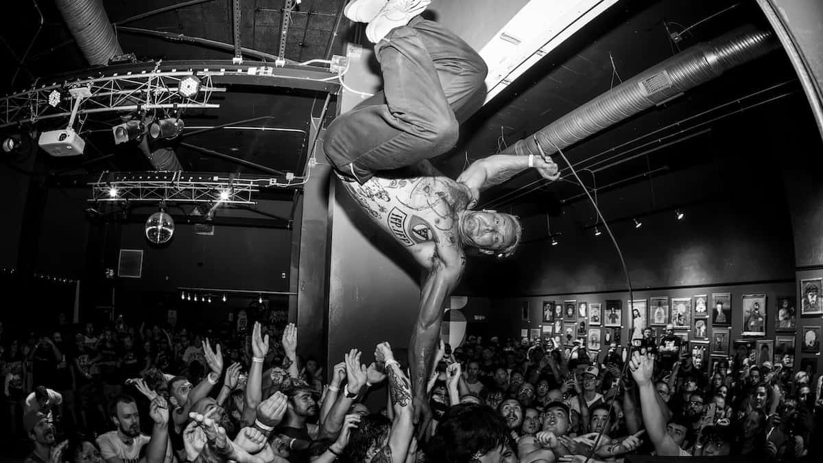 Foto en blanco y negro de un show de Haywire: un integrante salta sobre el público desde el escenario de un club lleno, con los brazos de la gente en alto