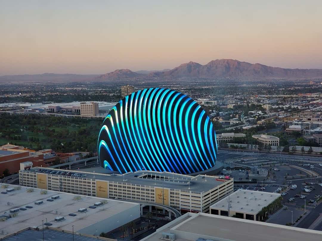 El edificio de la Sphere de Las Vegas al atardecer, visto desde la vuelta al mundo High Roller, con su superficie de pantallas encendida con franjas azules y las montañas de fondo. Foto: Y2kcrazyjoker4, Wikimedia Commons, CC BY 4.0