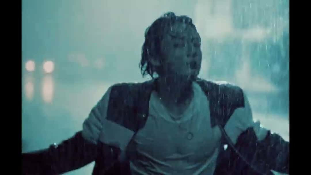 Fotograma del video oficial de «Seven»: Jungkook, empapado bajo la lluvia, con los brazos abiertos y una campera oscura