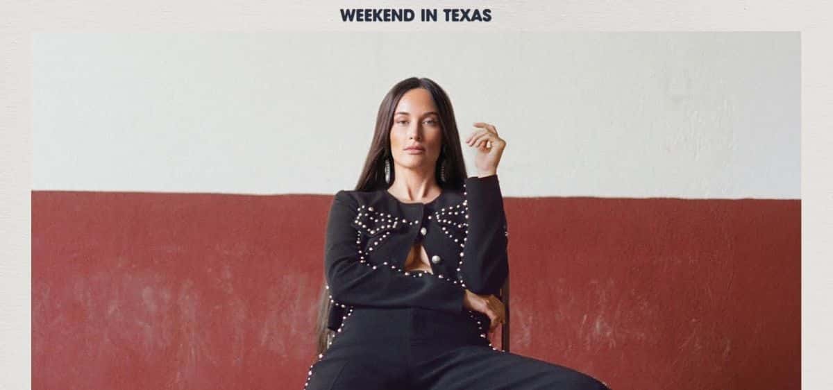 Arte oficial de «Weekend in Texas»: Kacey Musgraves, con pelo largo oscuro y un conjunto negro con apliques de perlas y un moño, sentada en una silla frente a una pared blanca y bordó