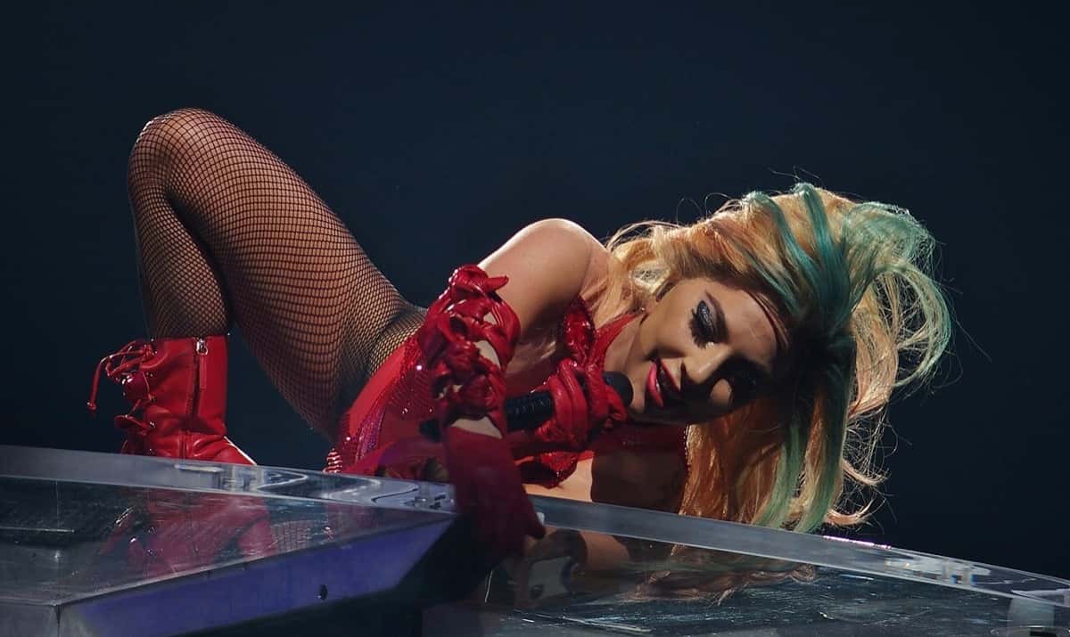 Lady Gaga canta arrodillada en el borde del escenario, con body rojo, medias de red y pelo rubio y verde, en el Joanne World Tour en Montreal, en 2017 (foto de archivo)
