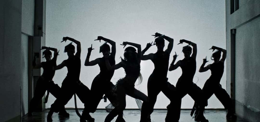 Fotograma de archivo del video de «SaWaDiKa»: siluetas negras de LISA y su cuerpo de baile haciendo la misma coreografía, con los brazos en alto, contra una pared blanca iluminada