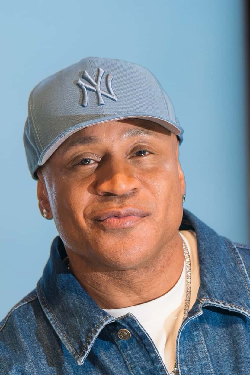 LL Cool J en octubre de 2026, con gorra celeste de los Yankees de Nueva York, campera de jean, remera blanca y una cadena plateada, sonriendo frente a un fondo celeste (foto de archivo). Foto: Colleen Sturtevant, CC BY-SA 4.0, vía Wikimedia Commons