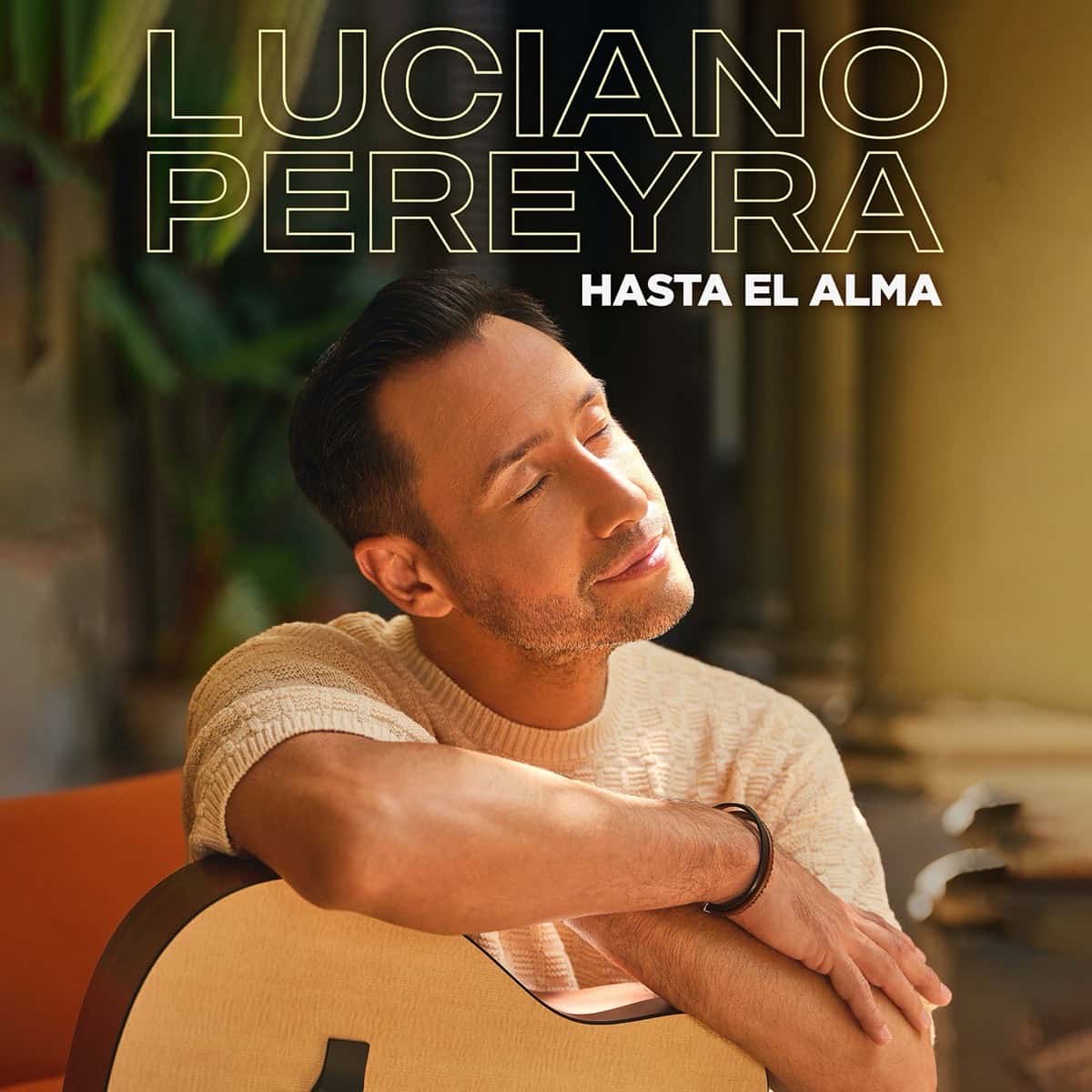 Portada de «Hasta El Alma», de Luciano Pereyra: el cantante, con los ojos cerrados y los brazos apoyados sobre una guitarra, en un ambiente cálido con plantas (foto de archivo)