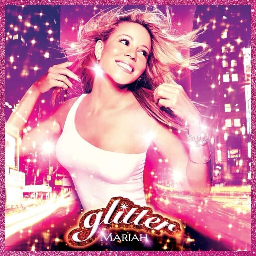 Portada oficial de «Glitter», de Mariah Carey: la cantante, con musculosa blanca y el pelo al viento, sonríe entre luces de ciudad y destellos rosas, con el logo «glitter» en letras brillantes rojas y blancas abajo