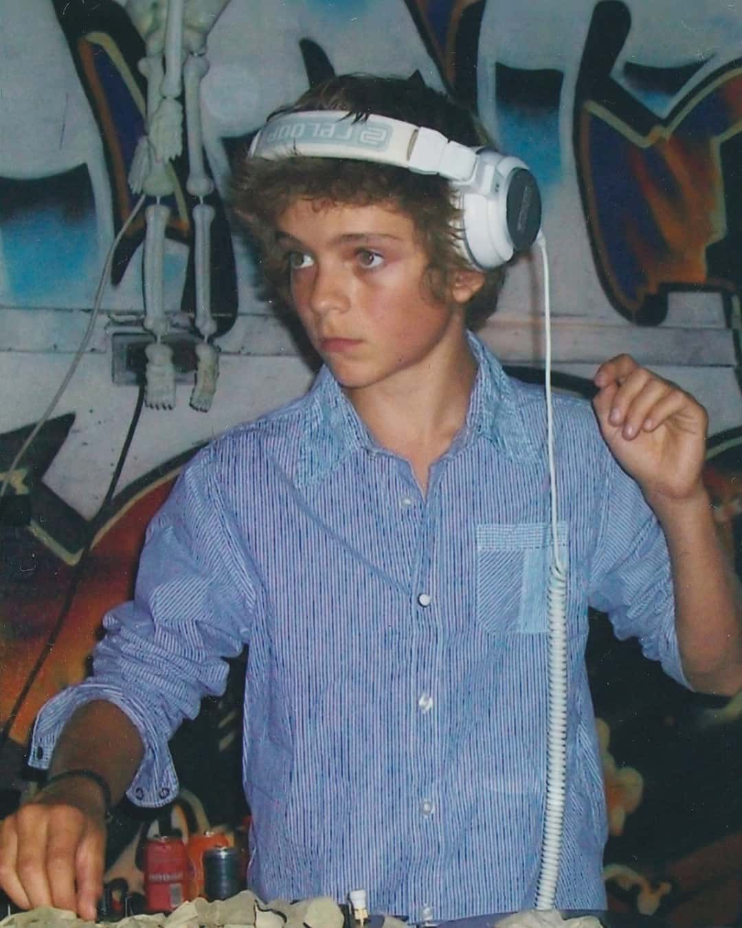 Martin Garrix de chico, en sus comienzos como DJ Marty, con auriculares blancos y camisa celeste, pinchando frente a una pared con grafitis (foto de archivo difundida por el artista)