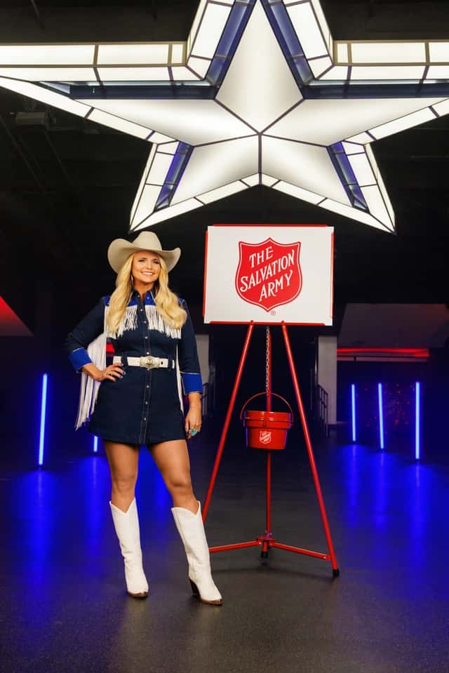 Miranda Lambert, con sombrero blanco, vestido corto de jean con flecos y botas blancas, posa junto a una olla roja del Ejército de Salvación bajo una estrella iluminada de los Cowboys. Foto: Ejército de Salvación / Dallas Cowboys