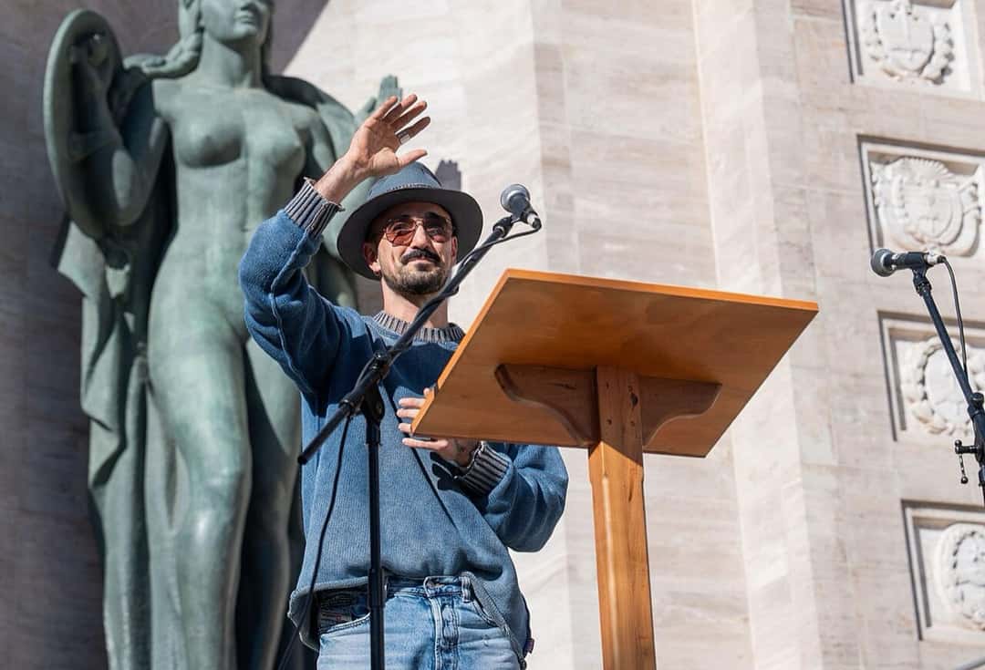 Abel Pintos, con sombrero, anteojos de sol y suéter azul, saluda con la mano en alto frente a un micrófono en el Monumento Nacional a la Bandera, en Rosario, en junio de 2026 (foto de archivo). Foto: Gobierno de Santa Fe, CC BY-SA 2.5, vía Wikimedia Commons