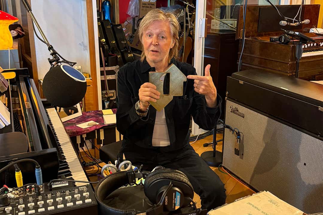 Paul McCartney en su estudio, sentado entre un piano, un micrófono y un amplificador, muestra el trofeo por el primer puesto de