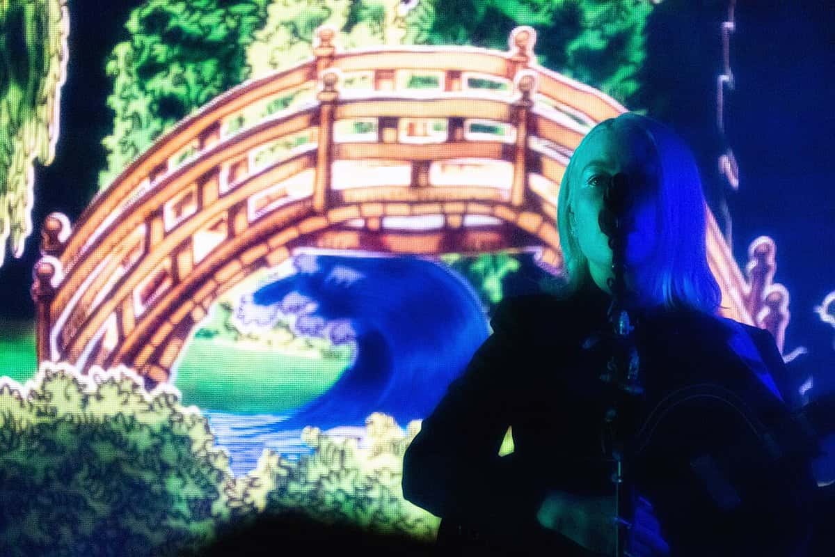 Phoebe Bridgers canta frente al micrófono, a contraluz, delante de una pantalla con un puente japonés y una ola en colores, en un show en Redmond, Estados Unidos (foto de archivo, agosto de 2022)