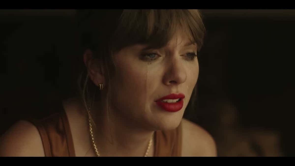 Fotograma del video oficial de "Patient Zero": Taylor Swift en primer plano, con flequillo, labios rojos, aros dorados y lágrimas en la cara, sobre un fondo oscuro
