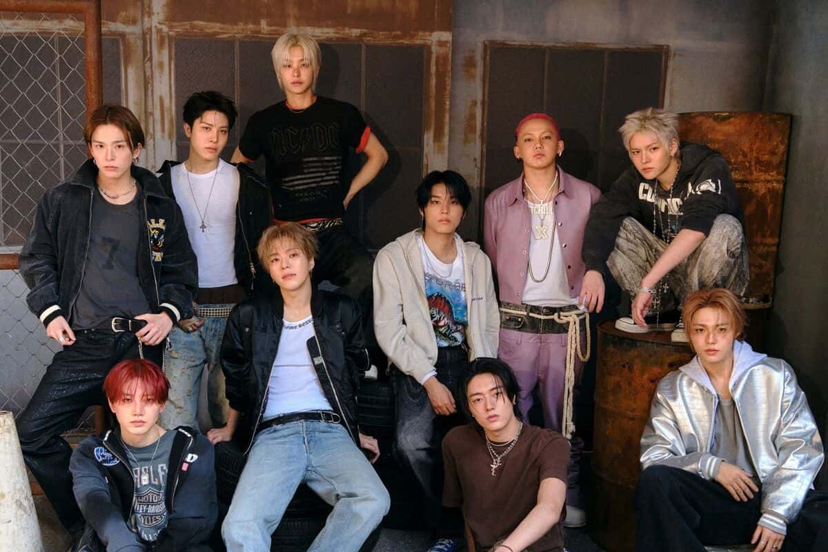 Foto de prensa de TREASURE: los integrantes del grupo posan en un galpón con paredes gastadas y barriles oxidados, con camperas, remeras y jeans (foto de archivo de la etapa «NEW WAV»)