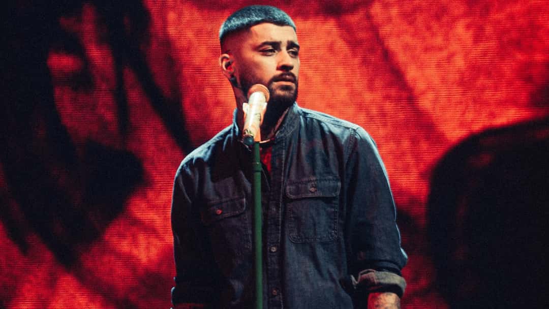 ZAYN cantando en vivo frente a un micrófono de pie, con camisa de jean, delante de una pantalla gigante con visuales en rojo, durante el show del 2 de octubre en Santiago de Chile. Foto: DG Medios / Andie Borie