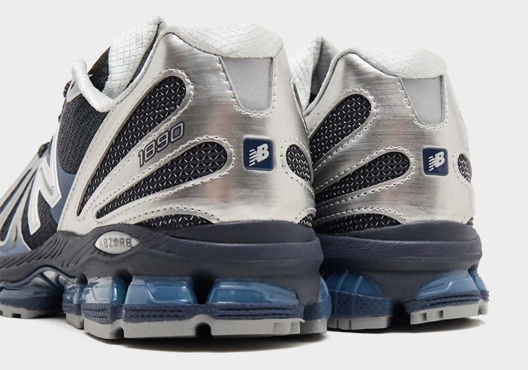 Vista trasera del par de New Balance 1890 Metallic Blue, con el talón plateado de textura cepillada, el número 1890, el logo de New Balance en un parche azul, la placa ABZORB y las cápsulas azules translúcidas sobre la suela gris