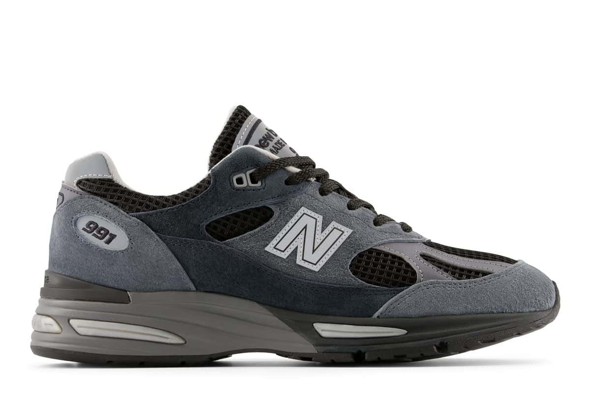 New Balance 991v2 Made in UK Turbulence de perfil, con gamuza azul grisácea y azul marino, malla negra, N gris claro y entresuela gris, sobre fondo blanco