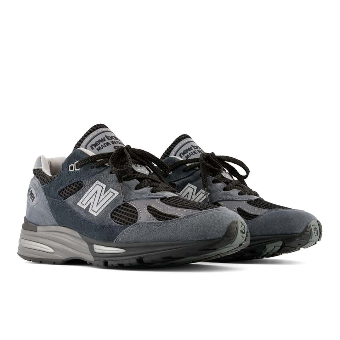 Par de New Balance 991v2 Made in UK Turbulence en vista diagonal, con gamuza en dos azules, malla negra y cordones negros