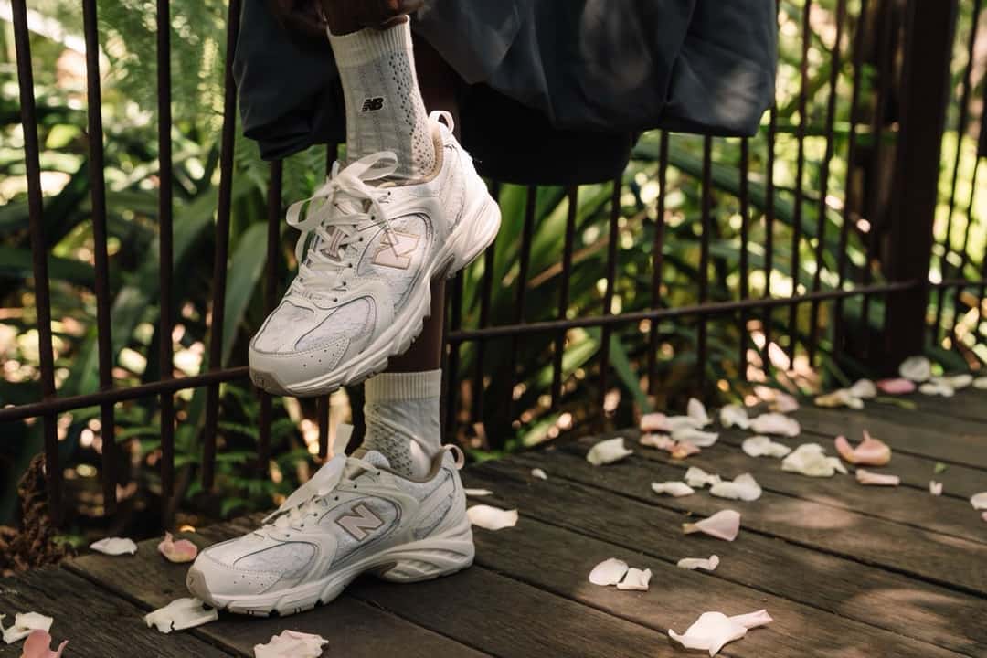 Pie con una New Balance del Sakura Pack en marfil con detalles rosa, apoyada sobre un escalón de madera con pétalos